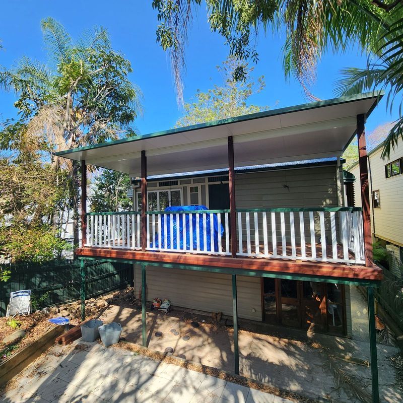 Elevated house with a deck. Green roof and railing, beige siding. Underneath is a concrete area.