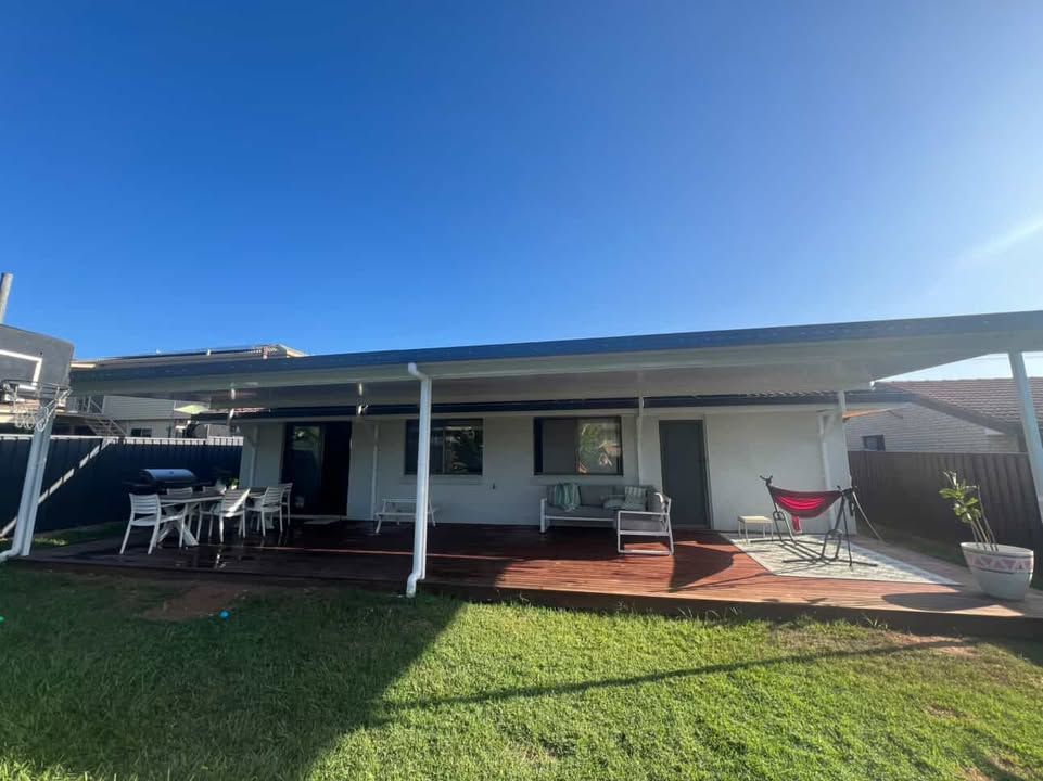 Backyard patio with a covered seating area, table, and chairs under a clear blue sky.