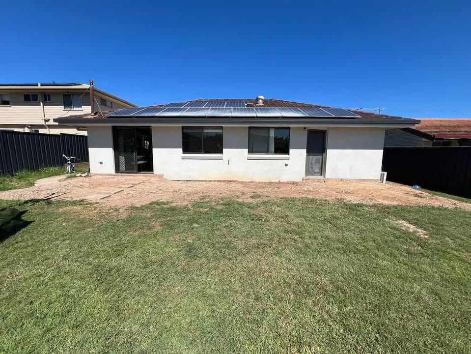 Backyard view of a white house with solar panels on the roof and a gravel patio area.