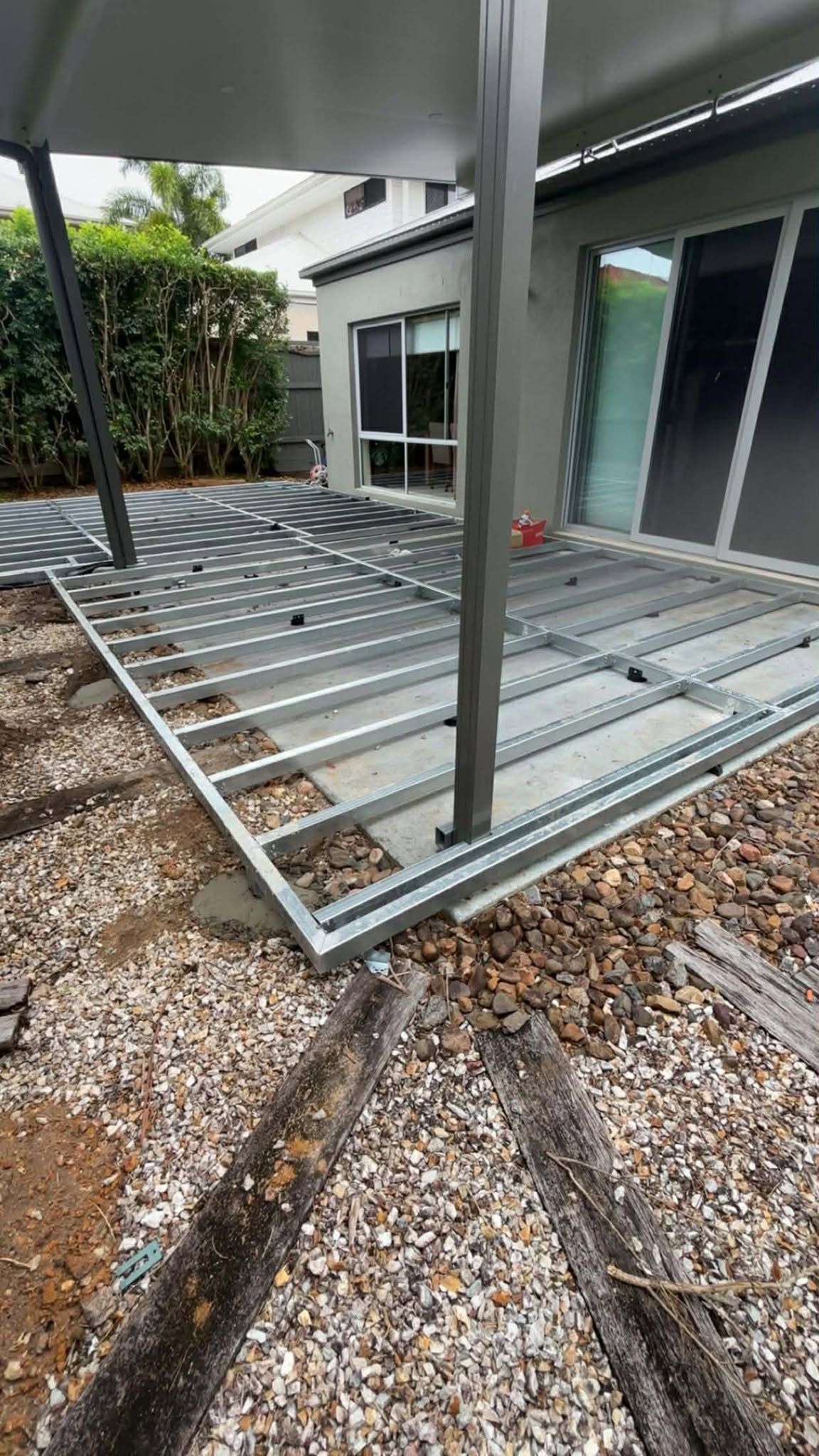 Metal deck frame construction with gravel ground, under a shaded pergola.
