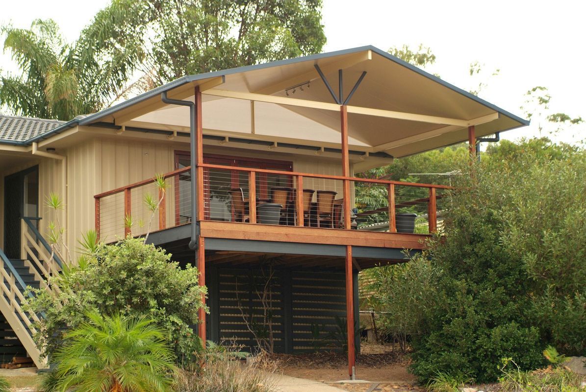 Deck with outdoor furniture under a covered patio, next to a house with wooden siding, surrounded by greenery.