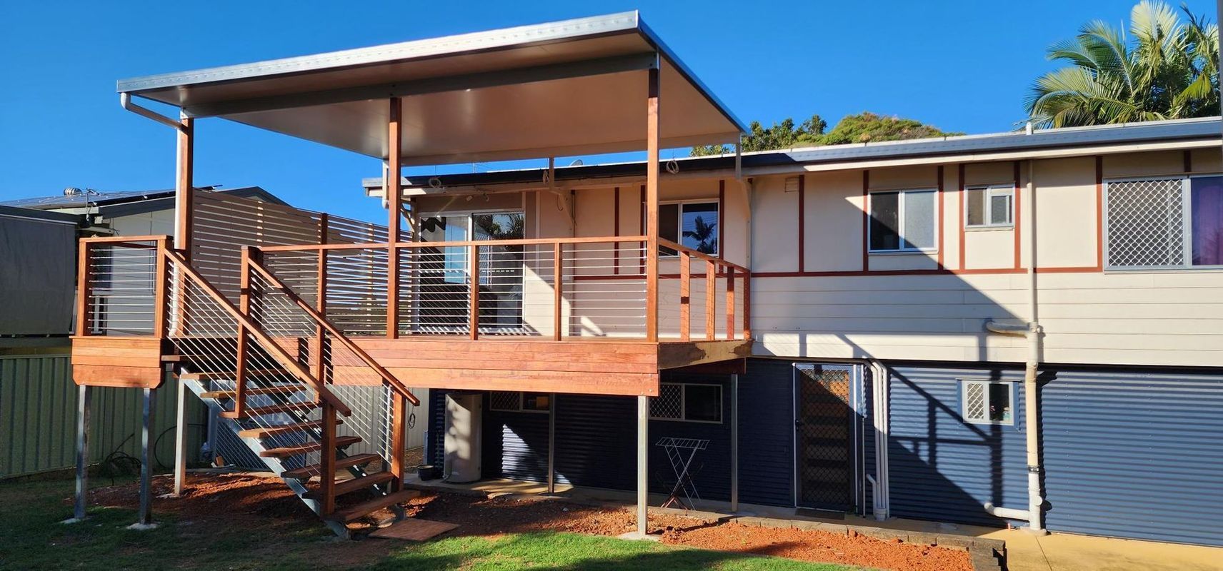 Wooden deck and stairs on a house with a covered patio. Blue sky and green grass visible.
