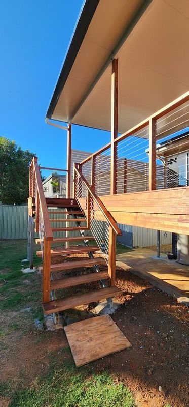 Wooden staircase leading up to a deck with cable railings and an overhang, set against a blue sky.