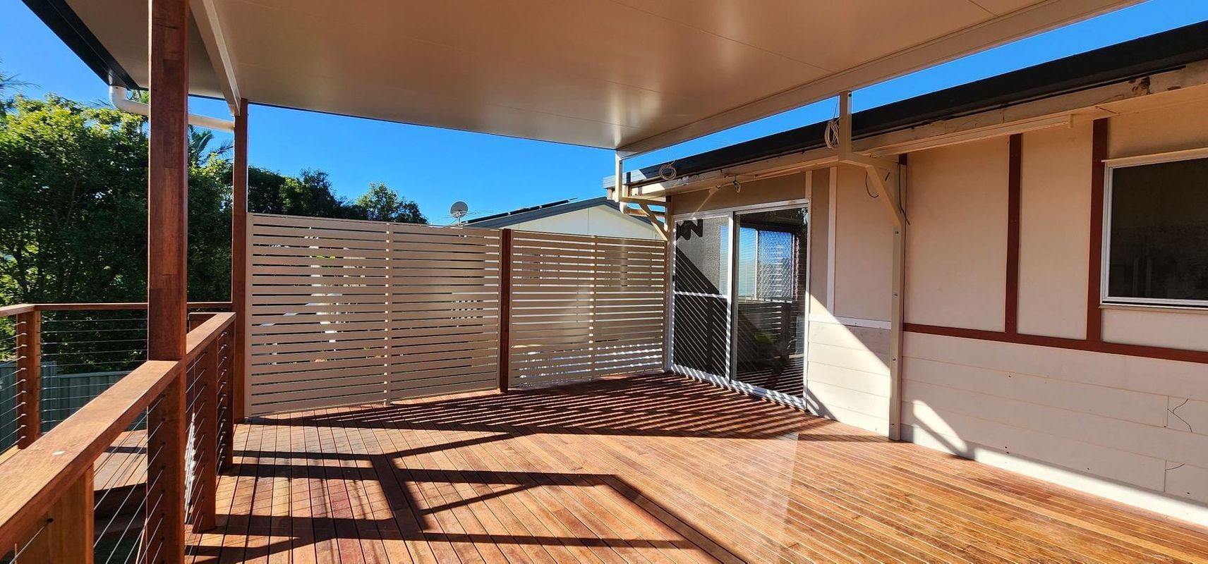 Wooden deck with a covered patio, fence, and a door leading inside. Sunny day, blue sky.