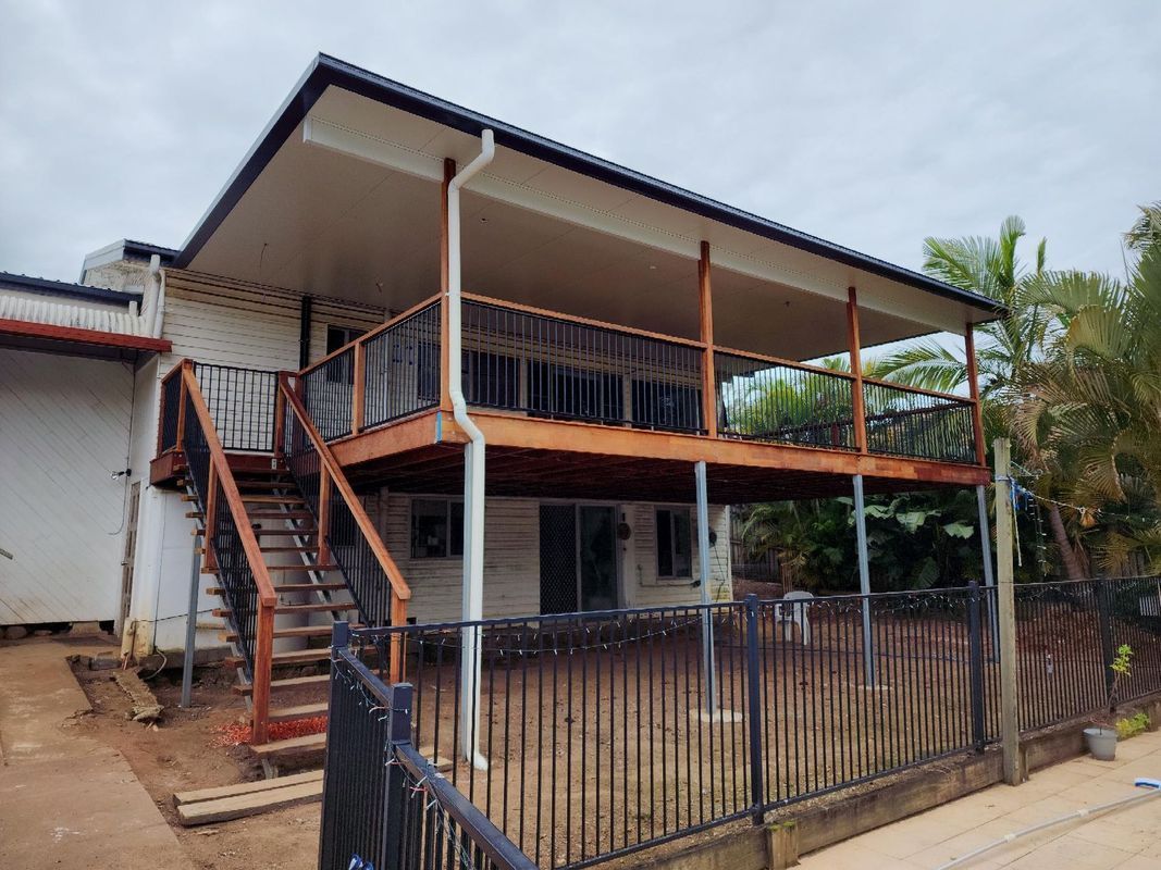Two-story house with wooden deck, stairs, and black railing. Overcast sky.