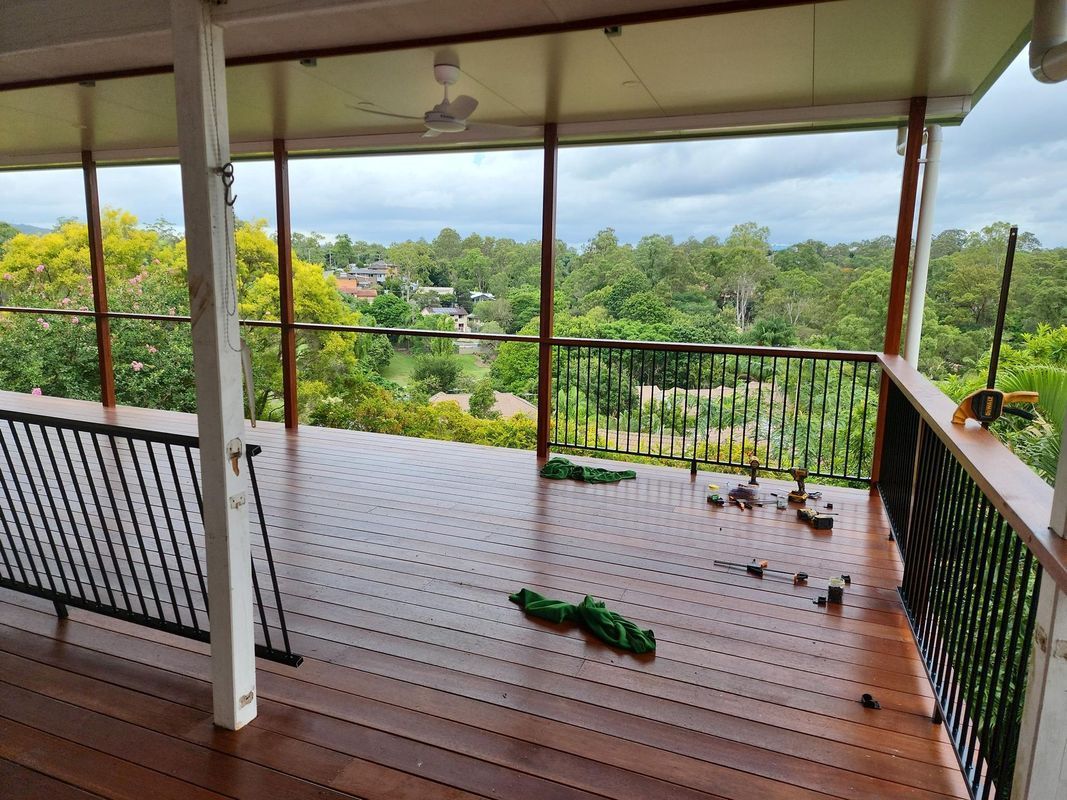 A wet wooden deck with black railings and a view of green trees under an overcast sky.