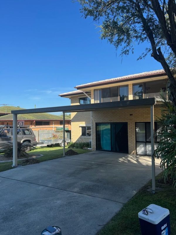 Two-story house with a carport; concrete driveway, green lawn, clear blue sky.