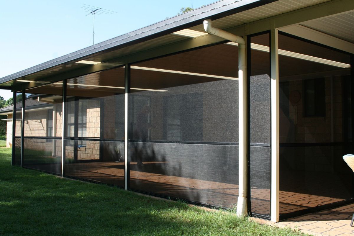 Black screen enclosure on a patio, under a roof, with green grass in the foreground.