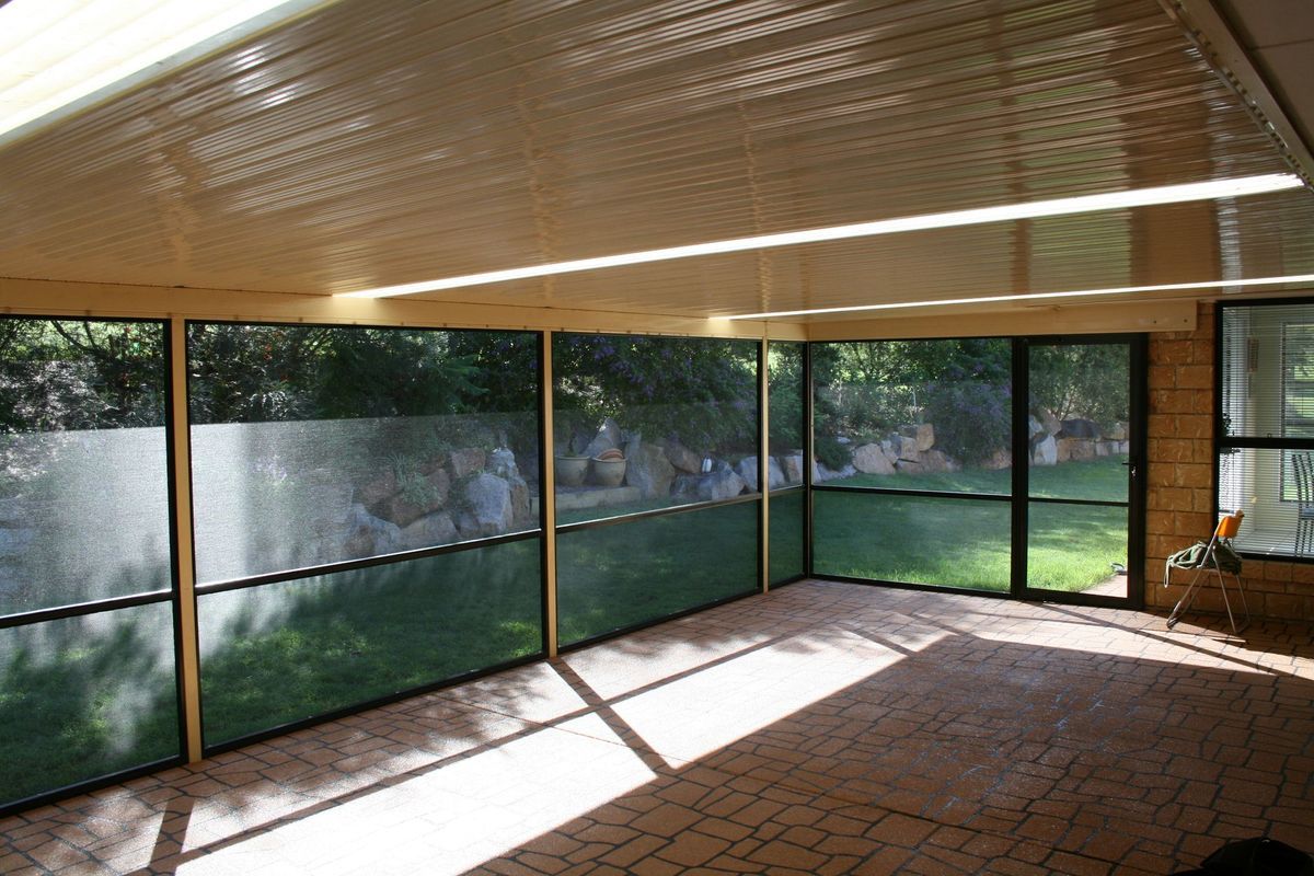 Sunroom with glass windows overlooking a grassy yard, beige ceiling, and sunlight streaming in.