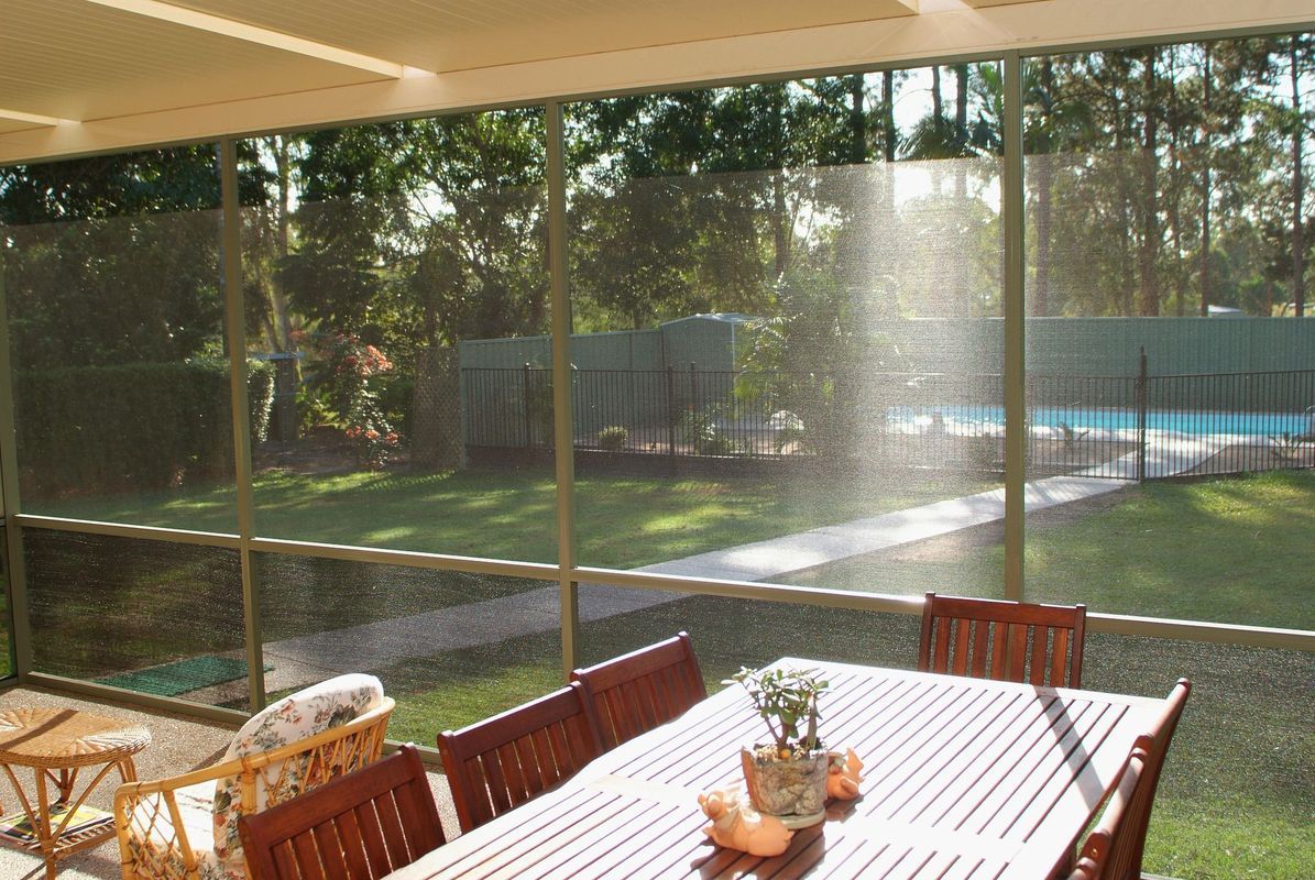 Outdoor dining area with a screen enclosure, looking out to a pool and trees.