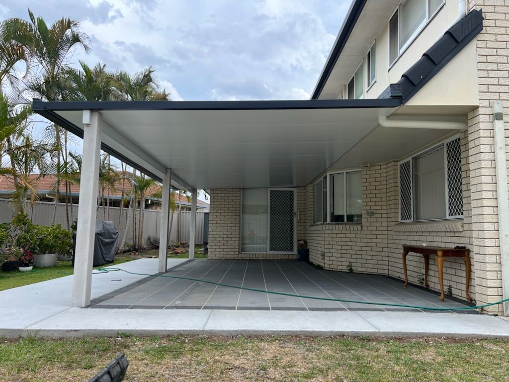 A patio with a gray tiled floor, attached to a brick house under a gray roof.
