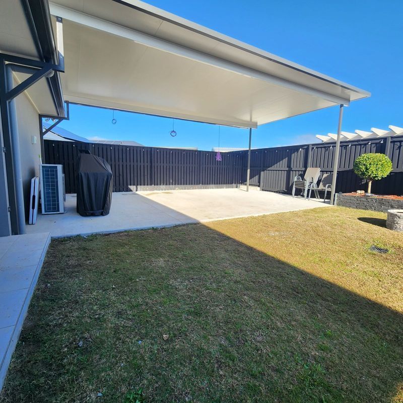 A backyard with a patio under a white awning, a grassy lawn, and a black fence.