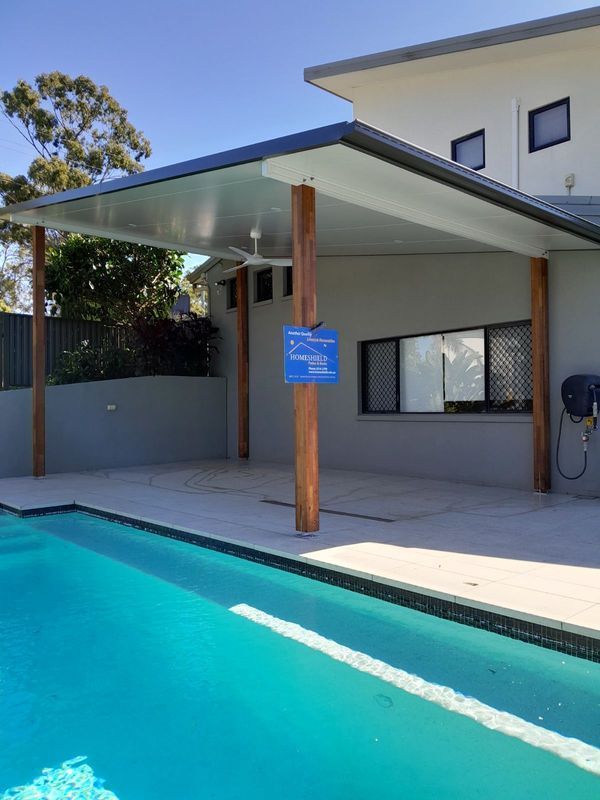 Poolside patio with blue pool and covered area with wooden supports.