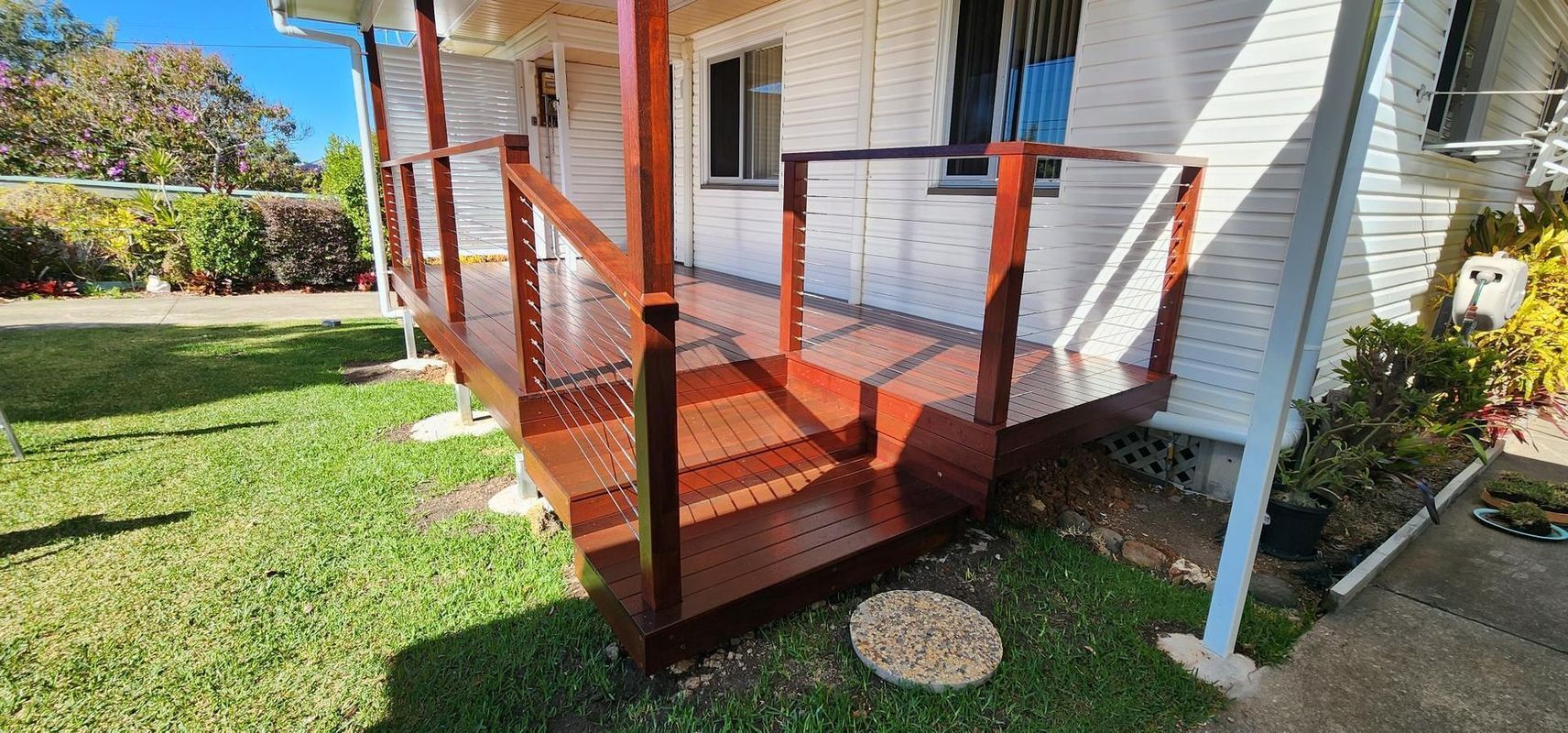 A freshly stained wooden porch with railings in front of a white house on a sunny day.