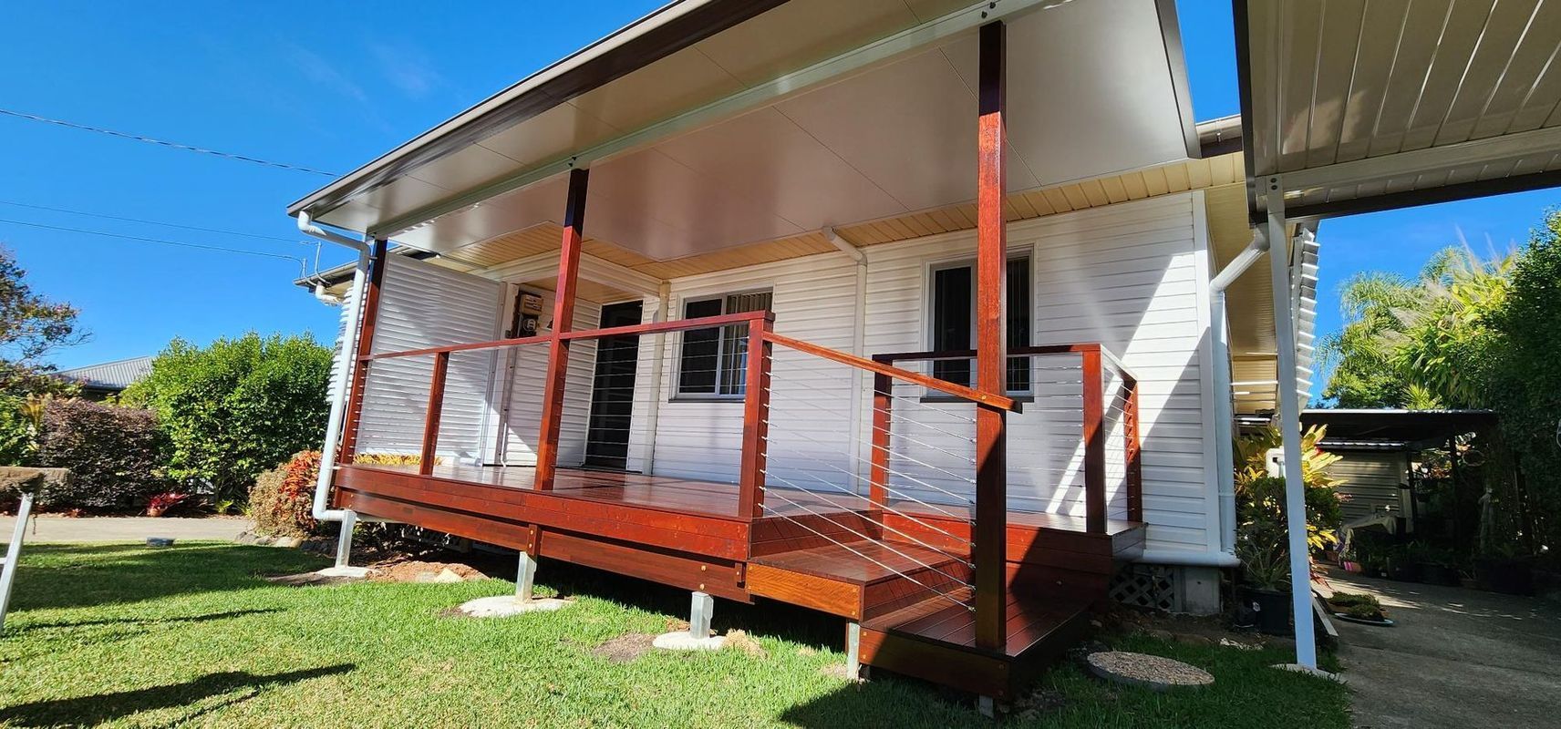 A wooden deck with a red-brown stain on a white house, under a covered patio.