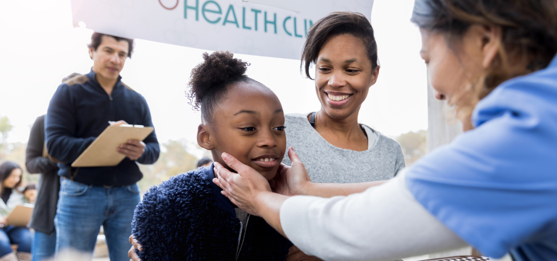 A photo of a nurse giving a check up o a young girl with her mother beside her at a clinic.