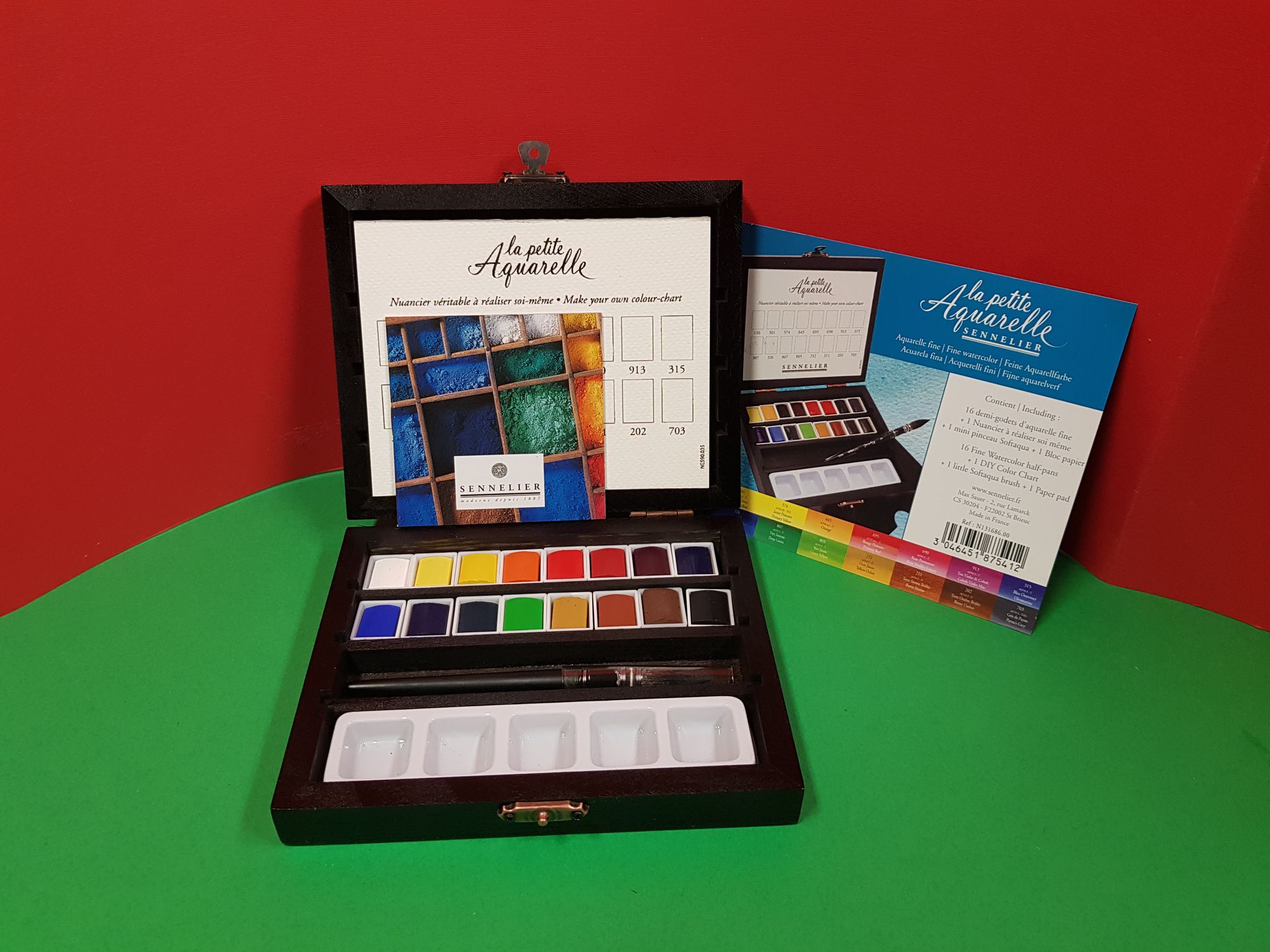 Set di acquerelli, aperto, con colori, pennello e tavolozza; scatola e coperchio sullo sfondo.