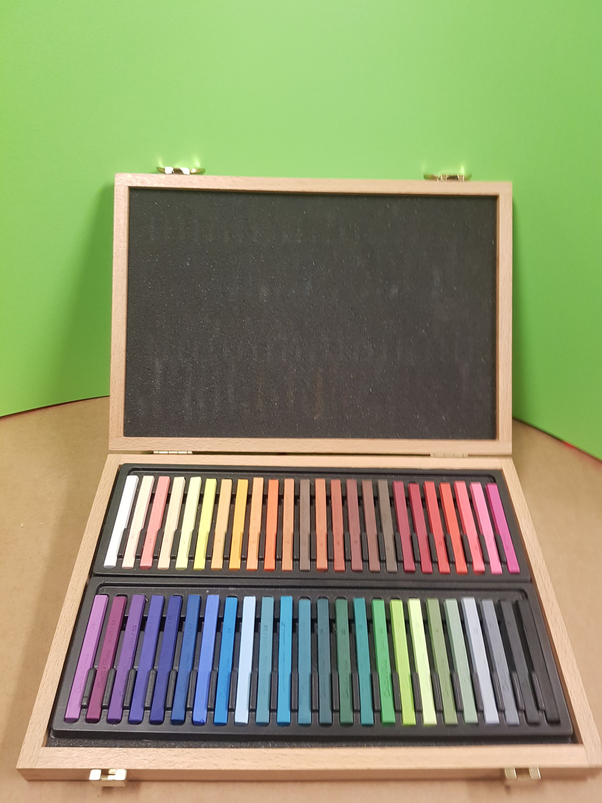 Scatola di legno contenente pastelli morbidi, aperta, che mostra file di gessetti di vari colori.