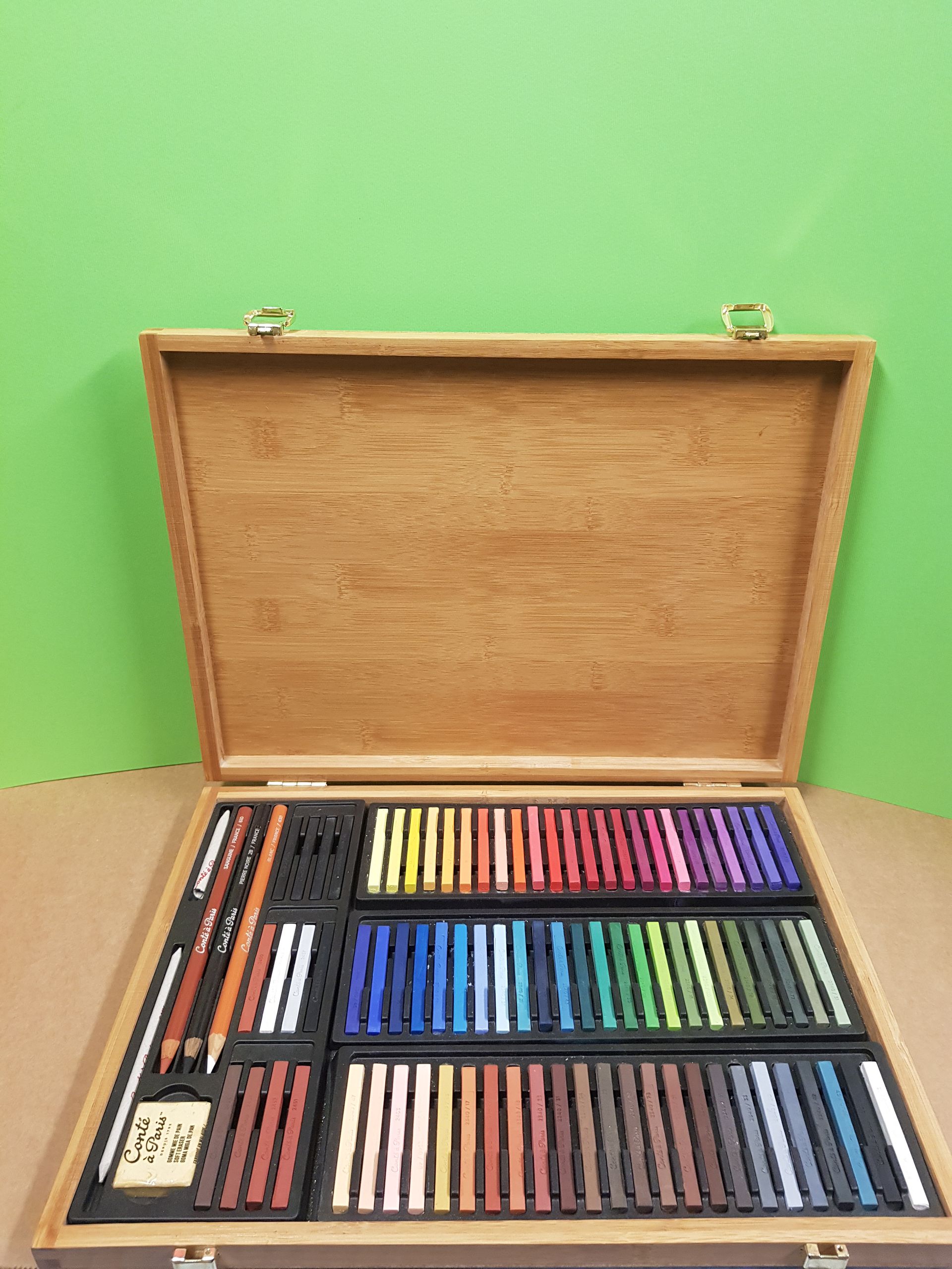 Valigetta in legno per opere d'arte aperta, piena di gessetti colorati e strumenti da disegno.