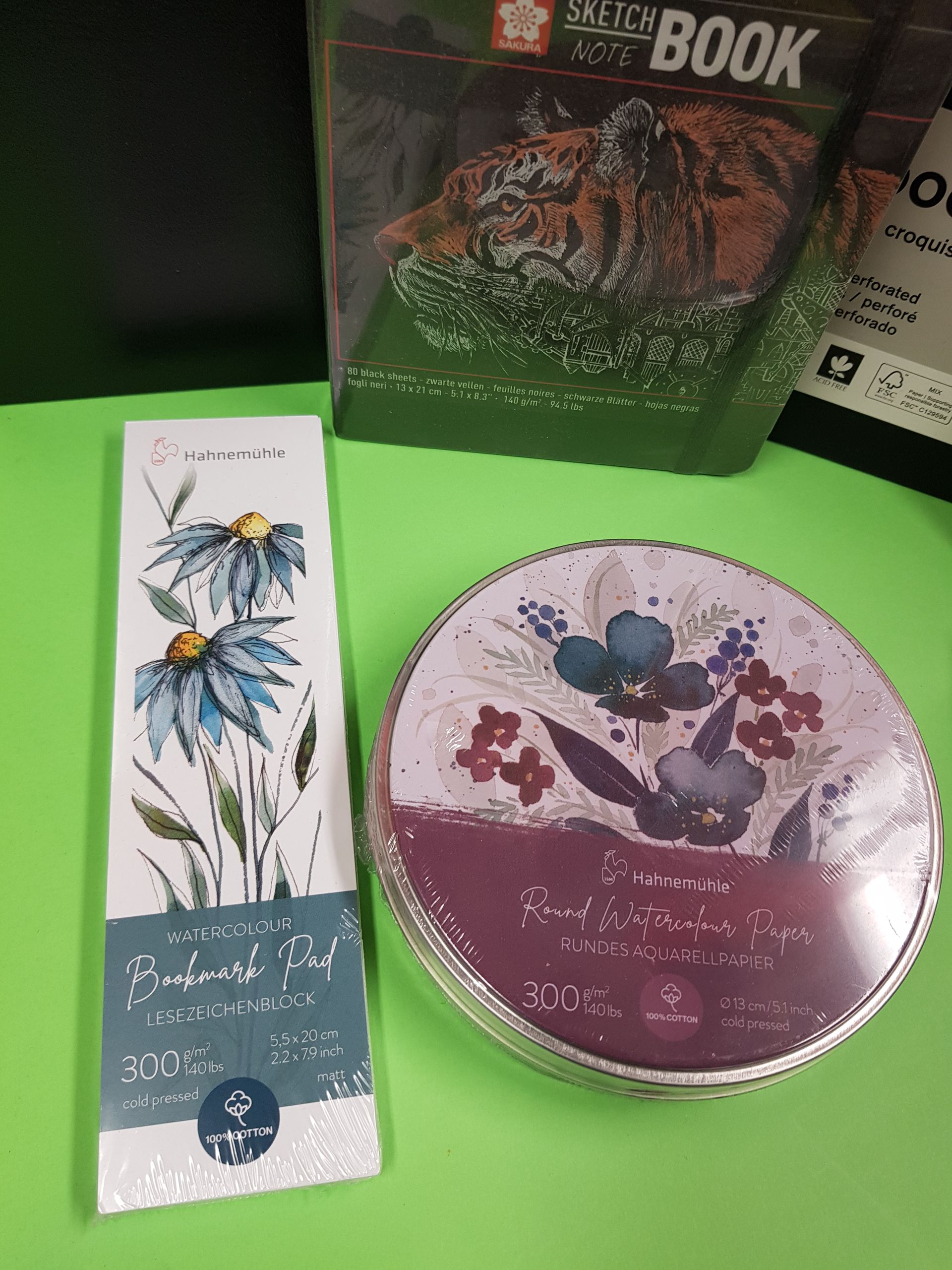 Oggetti su una superficie verde: segnalibro floreale, scatola rotonda e libro d'arte raffigurante una tigre.