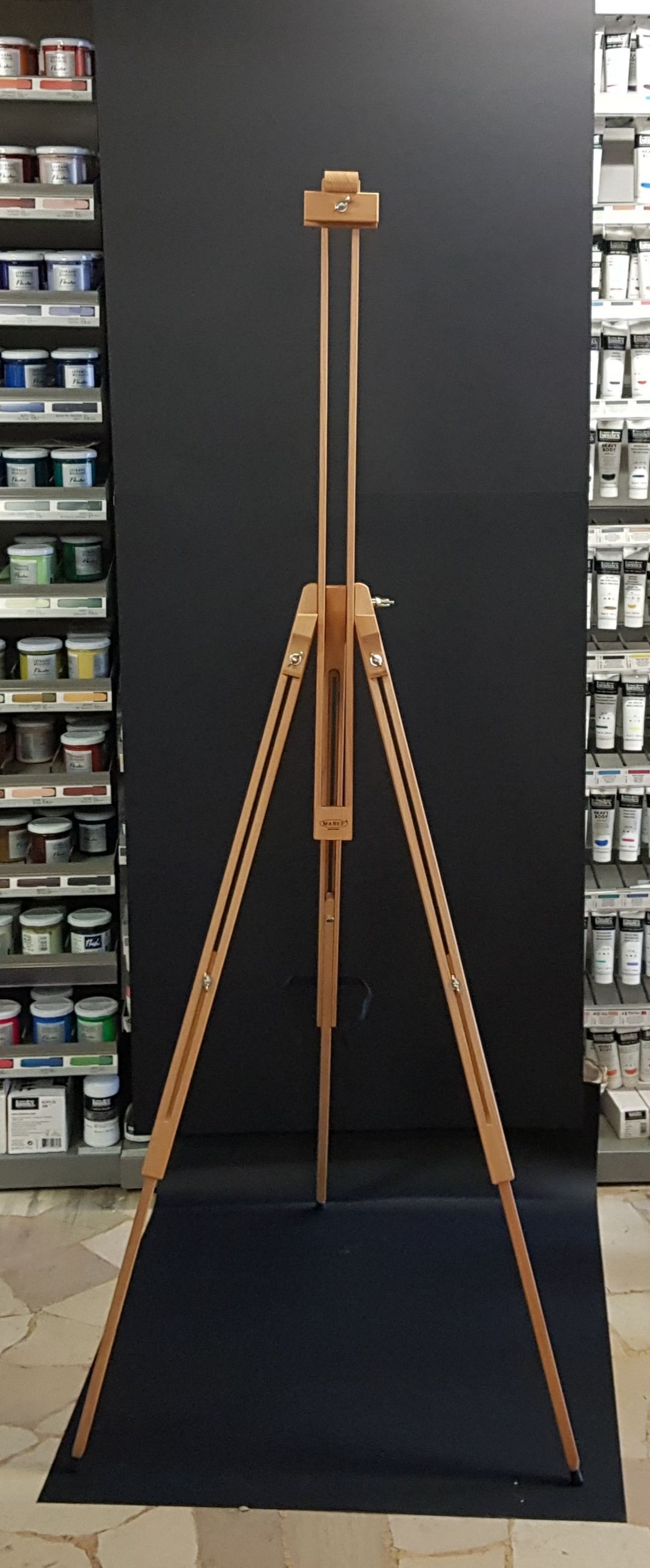 Cavalletto da artista in legno su una superficie blu scuro, con ripiani di materiale artistico su entrambi i lati.