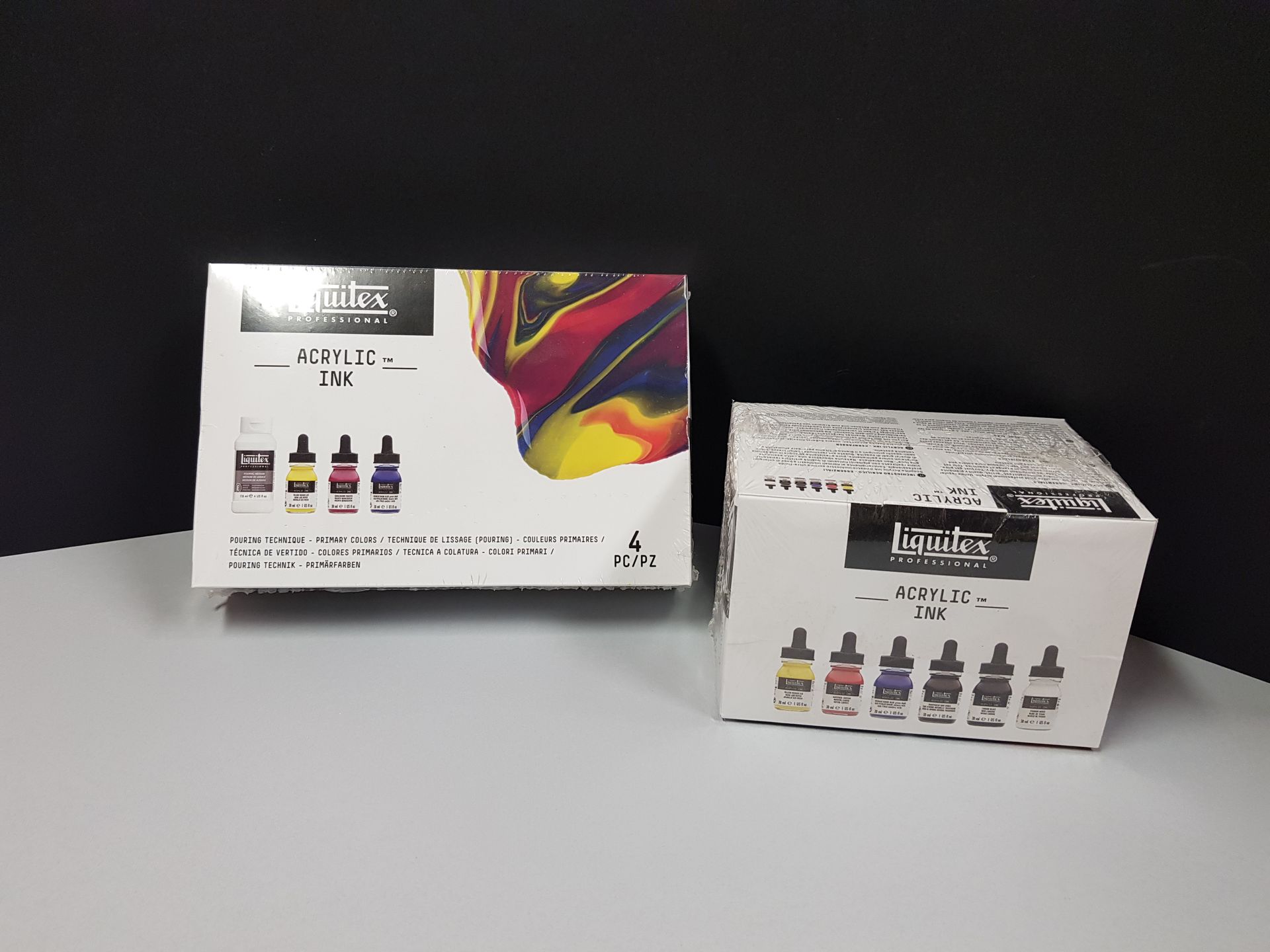 Due scatole bianche di inchiostri acrilici Liquitex su una superficie bianca, con uno sfondo nero.