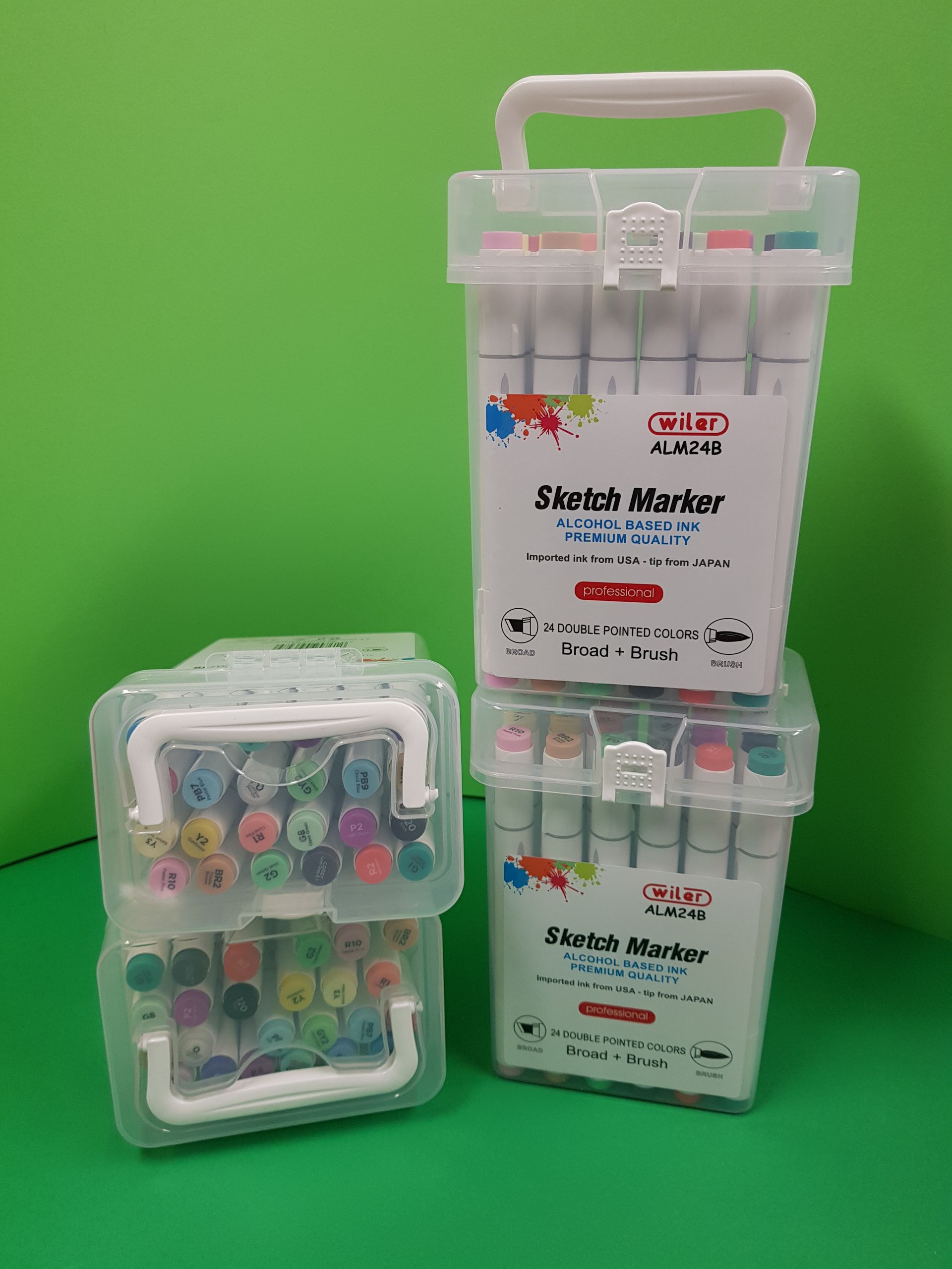 Tre set di pennarelli artistici colorati in custodie di plastica trasparente su una superficie verde.