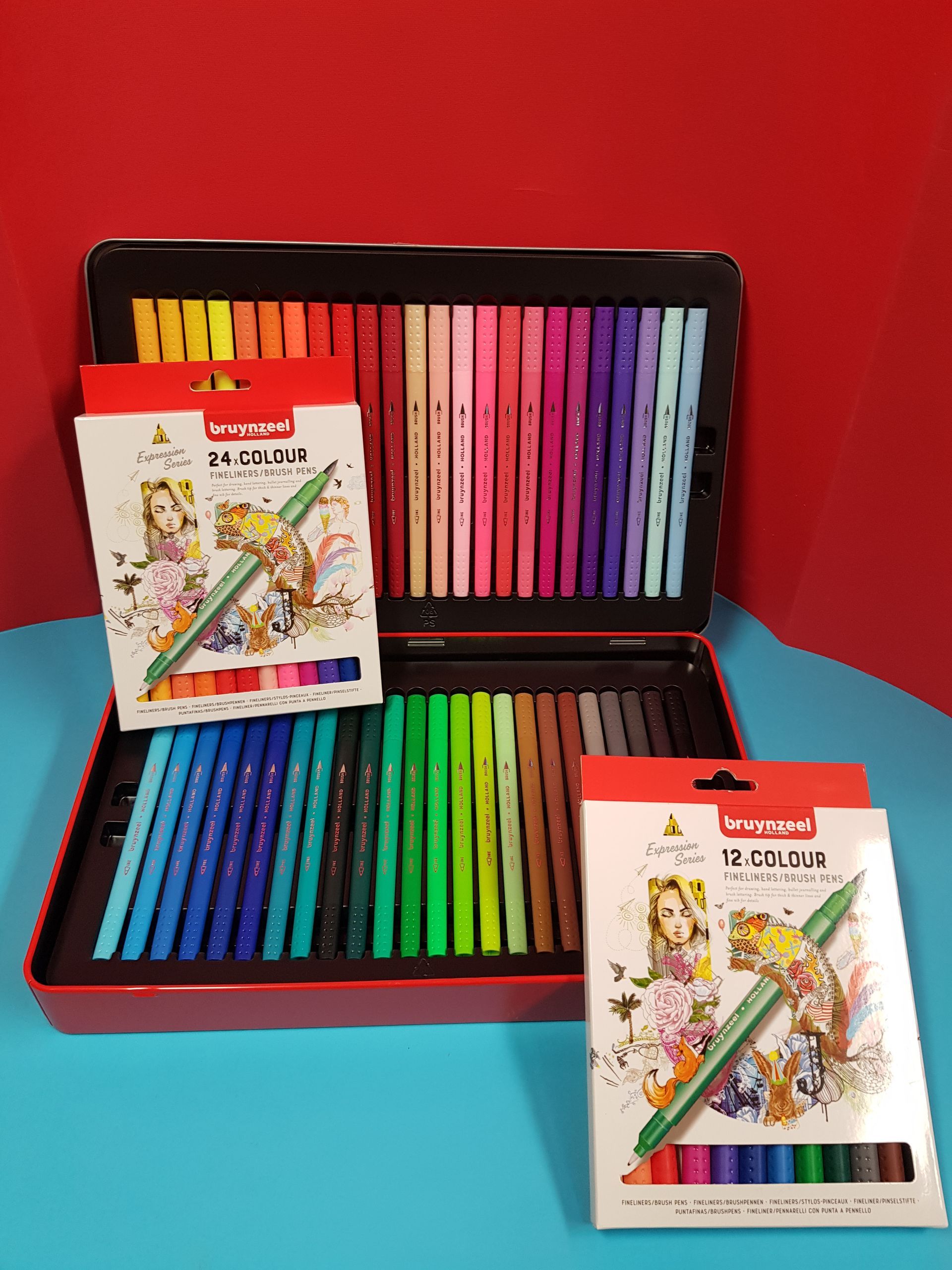 Astuccio rosso aperto pieno di pennarelli colorati, insieme a due set di pennarelli in scatola.