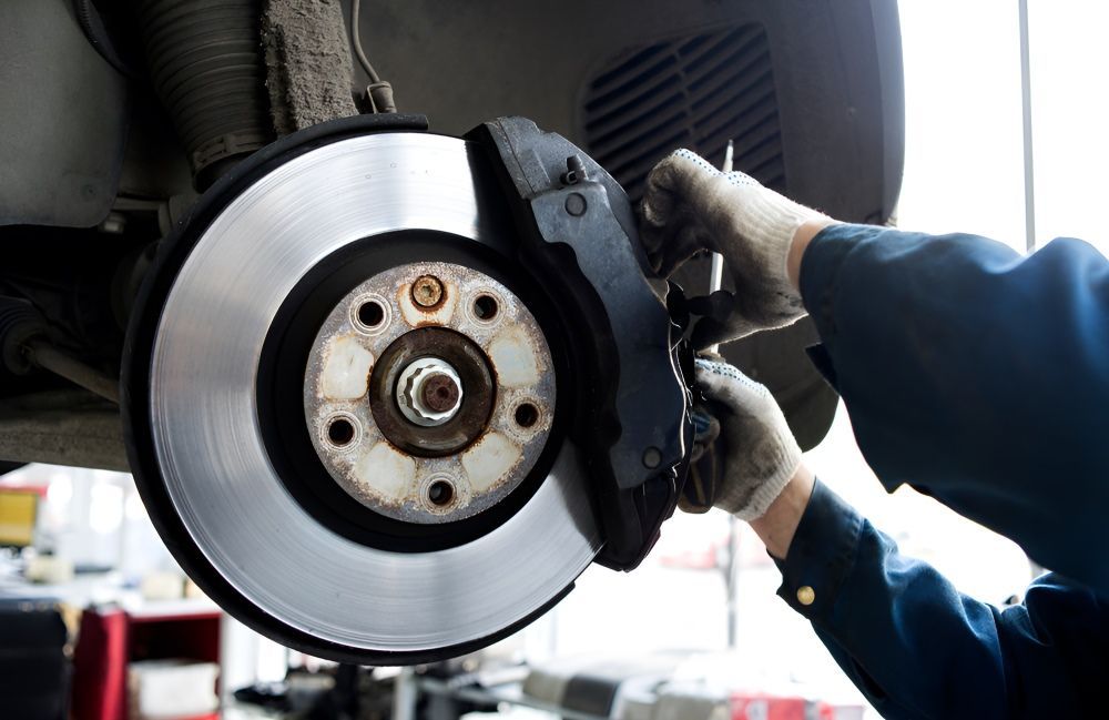 A Man Is Fixing A Brake Disc On A Car In A Garage — Tuned Suspension & Mechanical in Parkes, NSW