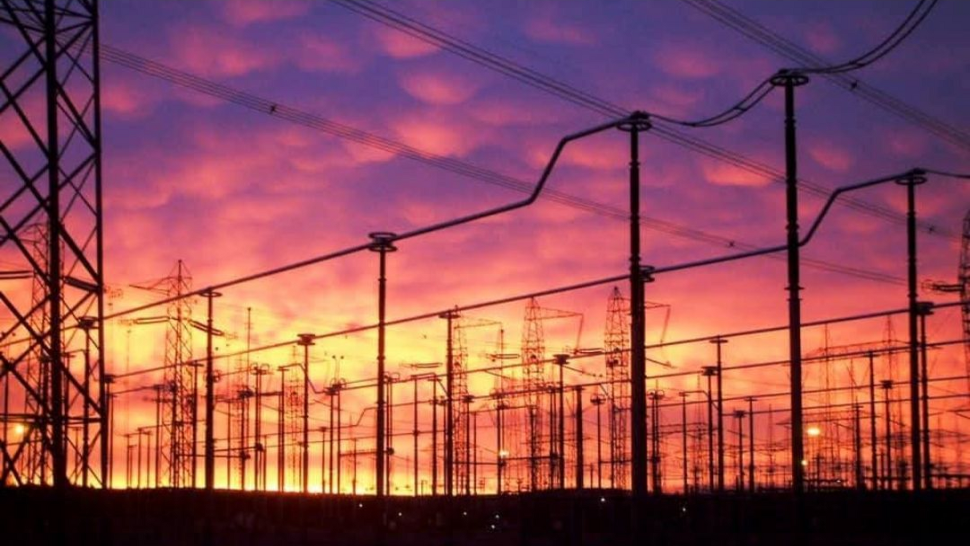Réseau électrique en silhouette sur fond de coucher de soleil aux teintes orange et violettes éclatantes.