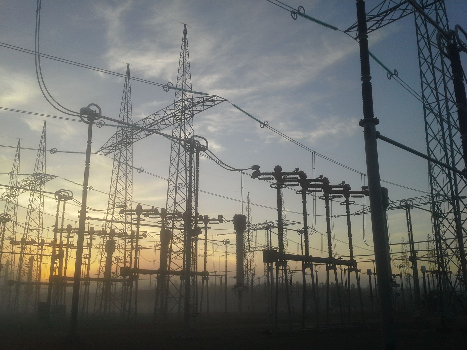 Les lignes électriques et les pylônes se découpent en silhouette sur le lever ou le coucher du soleil, créant une scène spectaculaire et contrastée.