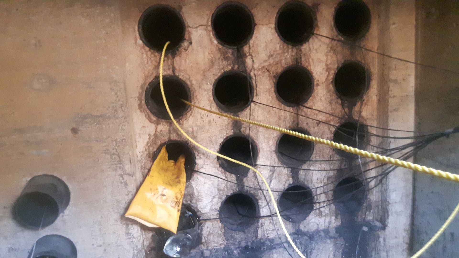 Mur percé de nombreux trous circulaires sombres, traversés par des fils électriques jaunes.