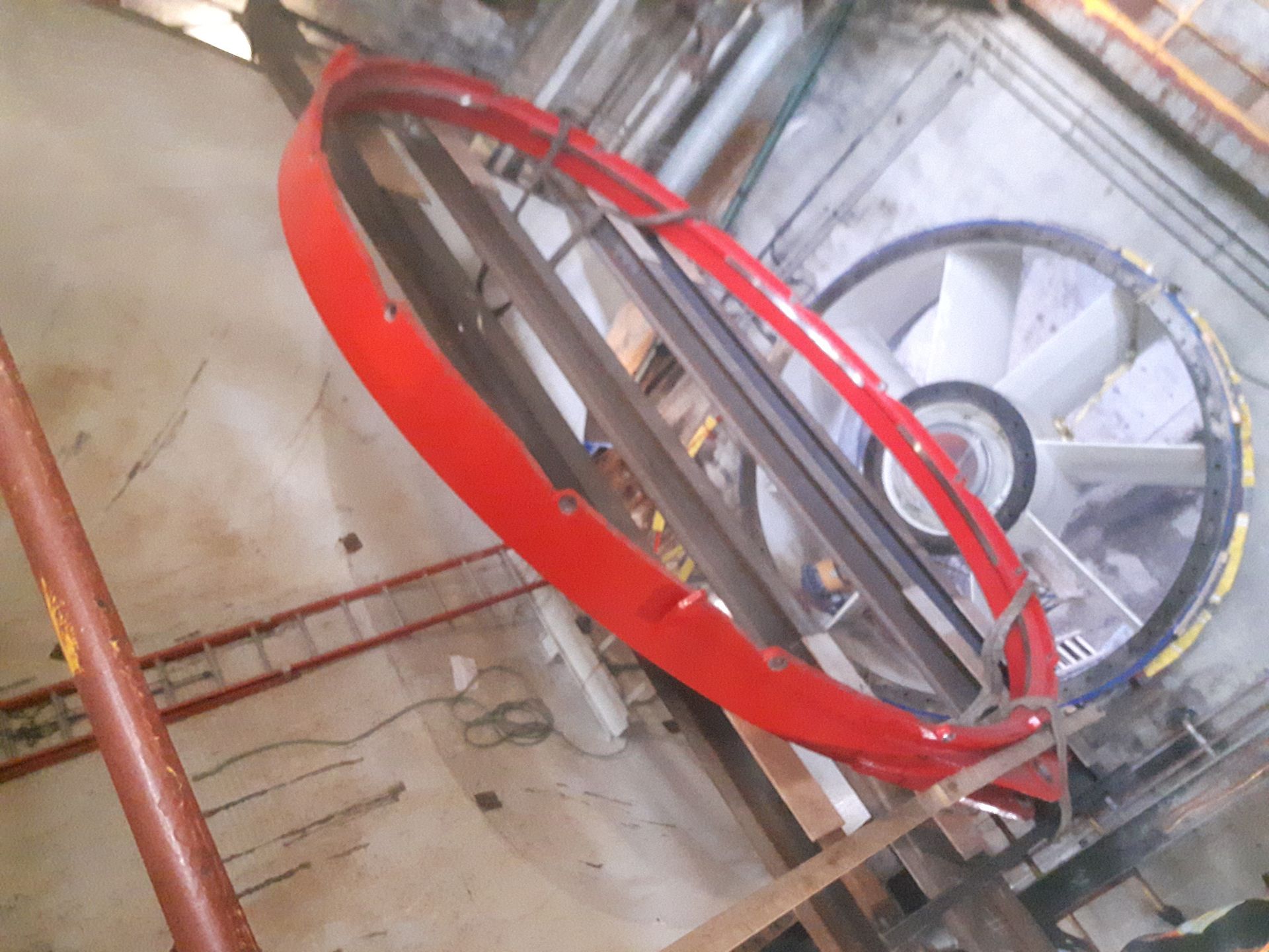 Structure annulaire rouge entourant un grand ventilateur à pales blanches, fixée au mur.