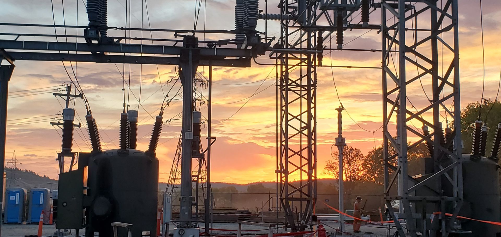 Poste de transformation électrique avec de hautes structures métalliques se détachant sur un coucher de soleil coloré.