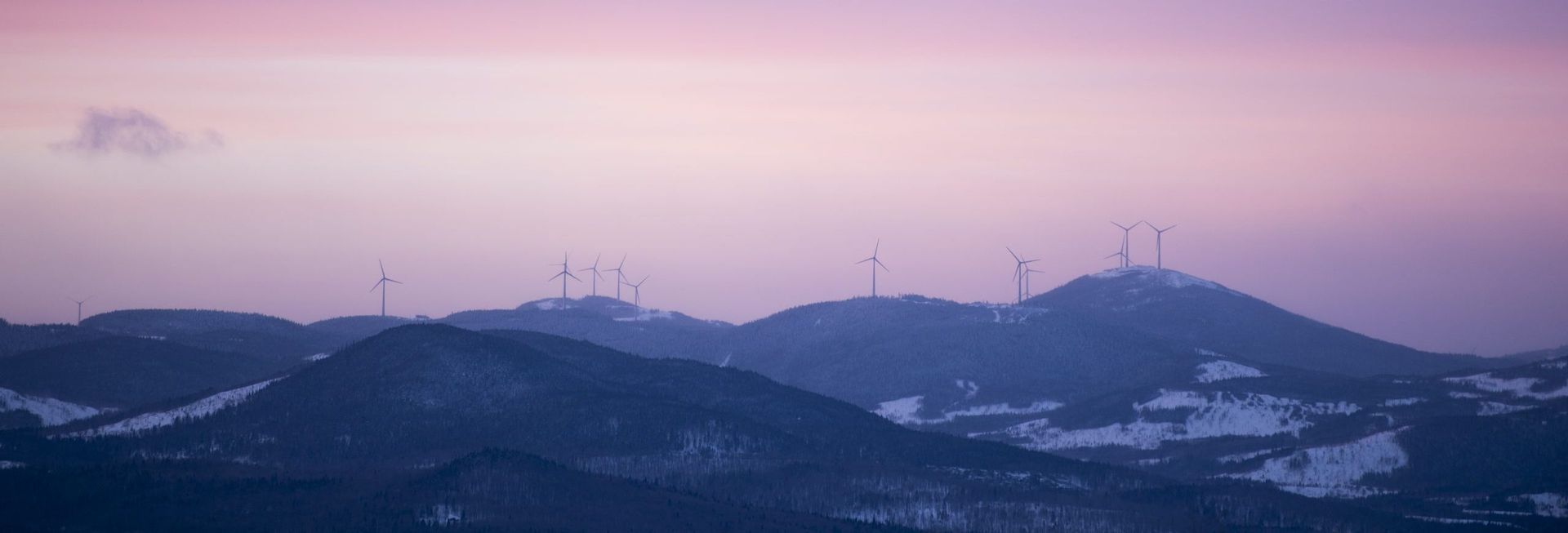 Éoliennes sur des collines enneigées sous un ciel rose et violet au crépuscule.