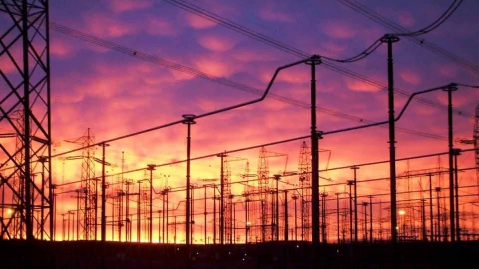 Réseau électrique en silhouette sur fond de coucher de soleil aux teintes orange et violettes éclatantes.