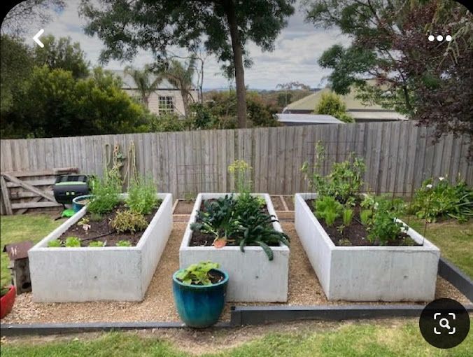 A row of concrete planters filled with plants in a garden.