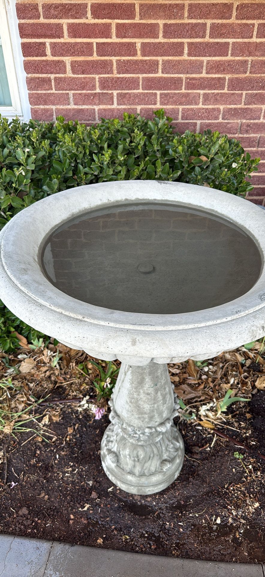 A blue jay is perched on top of a bird bath.