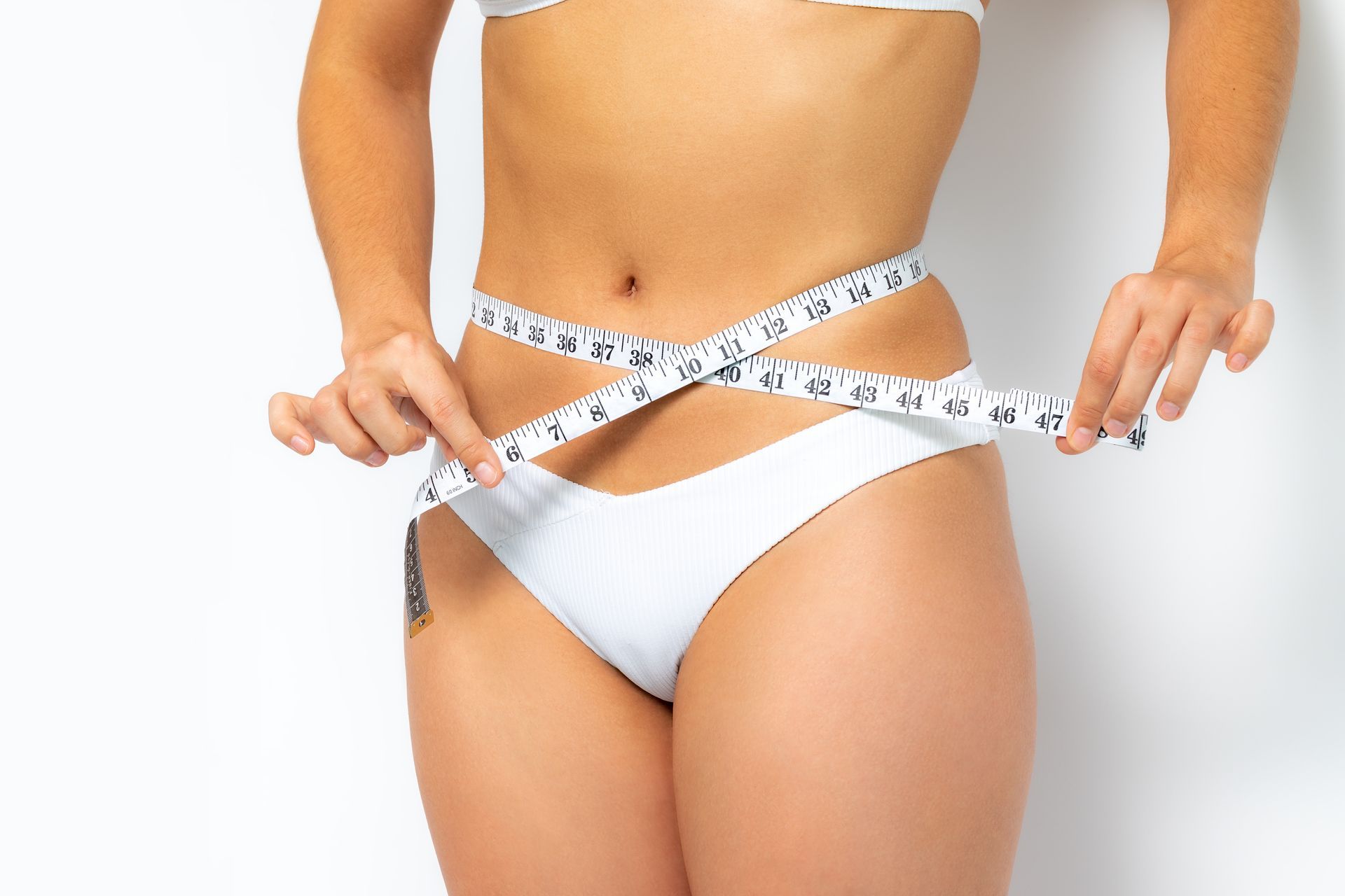 A woman in a bikini is measuring her waist with a tape measure.