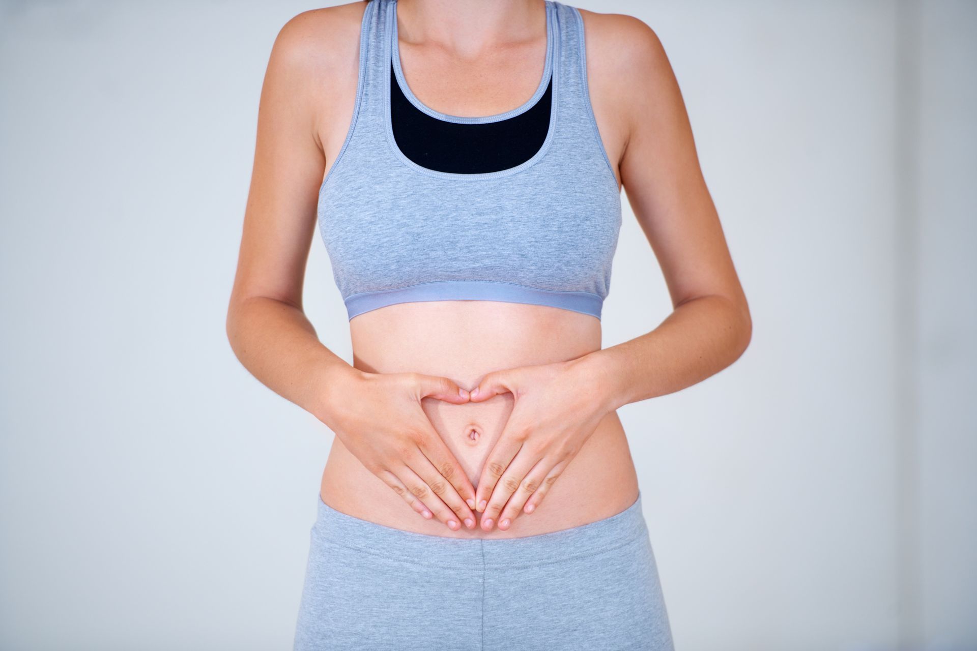 A woman is making a heart shape with her hands on her stomach.