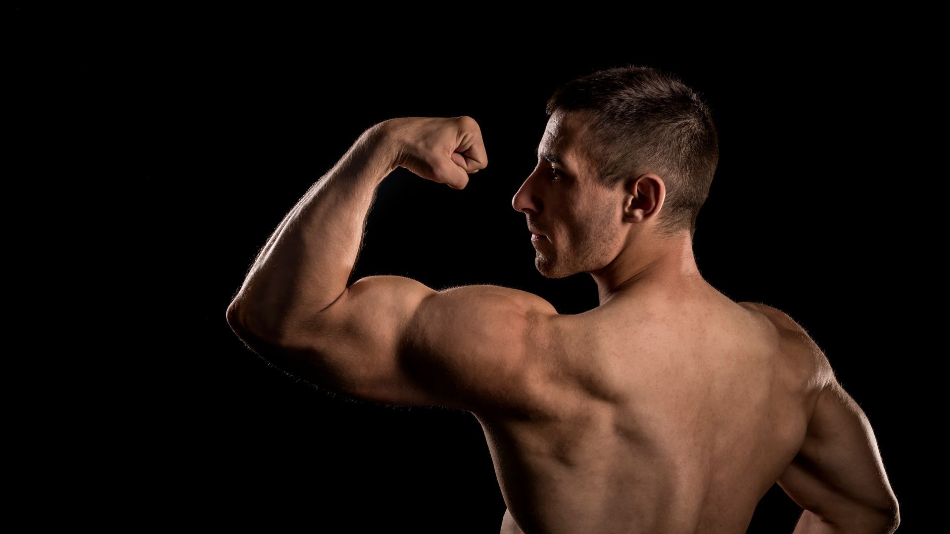 A shirtless man is flexing his muscles on a black background.