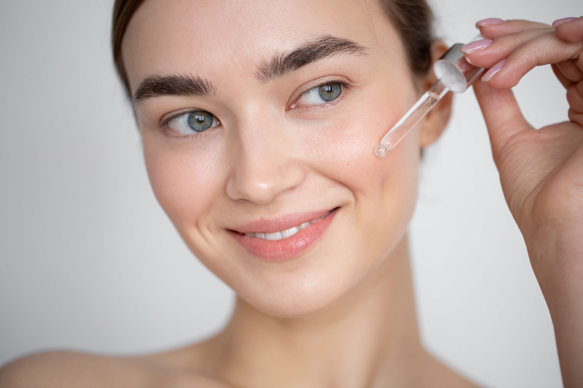 A woman is applying a serum to her face with a pipette.