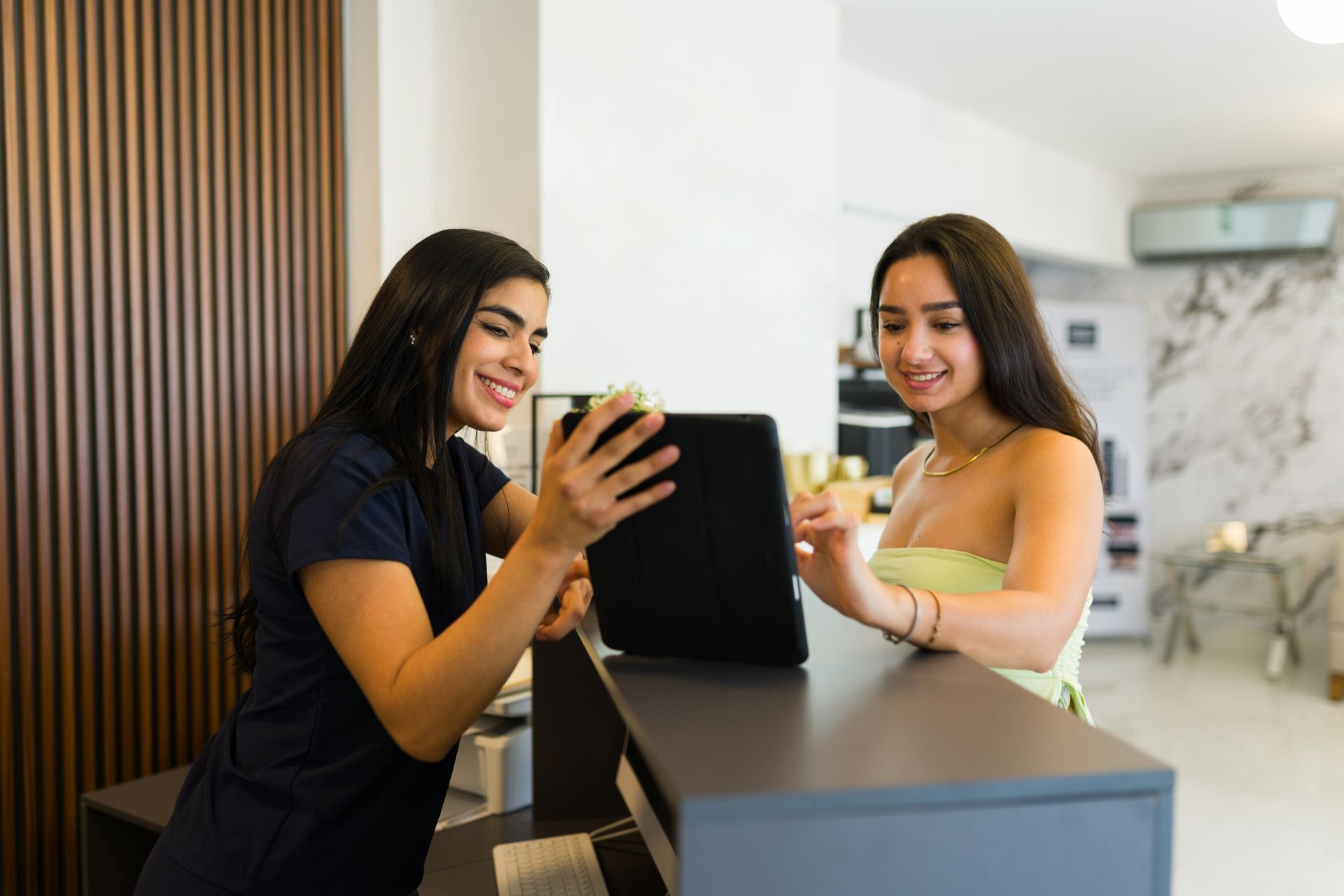 Two women are sitting at a counter looking at a tablet.