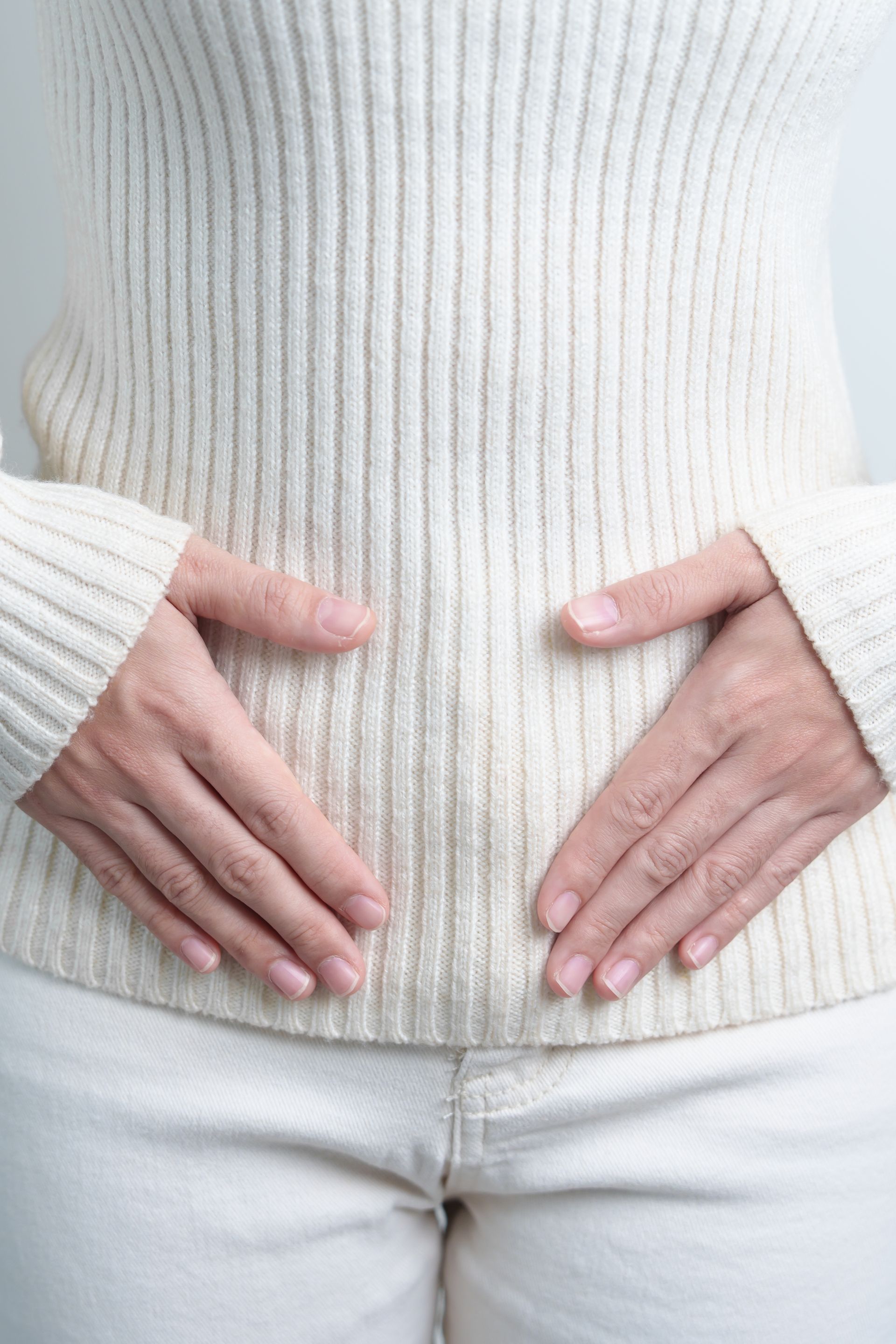 A woman in a white sweater is holding her stomach with her hands.