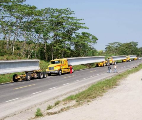 Una fila de camiones amarillos que transportan una viga muy larga por una carretera