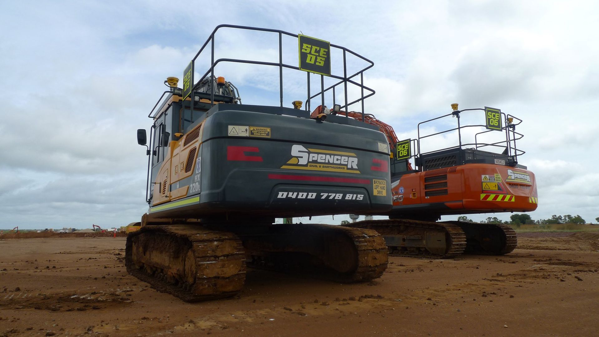 Two Spencer Civil & Earthworks excavators are parked next to each other in a dirt field.