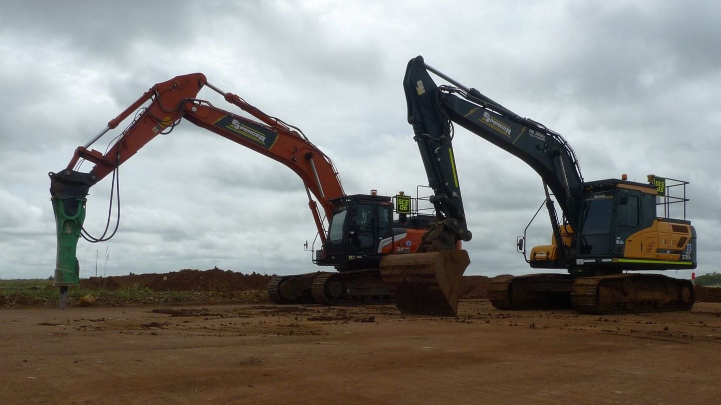 Two Spencer Civil & Earthworks excavators are resting next to each other on a flat dirt surface.
