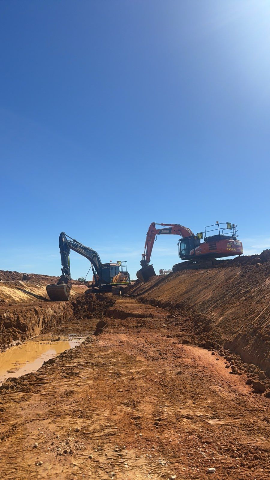 Two spencer civil & earthworks excavators are working on a drainage ditch.