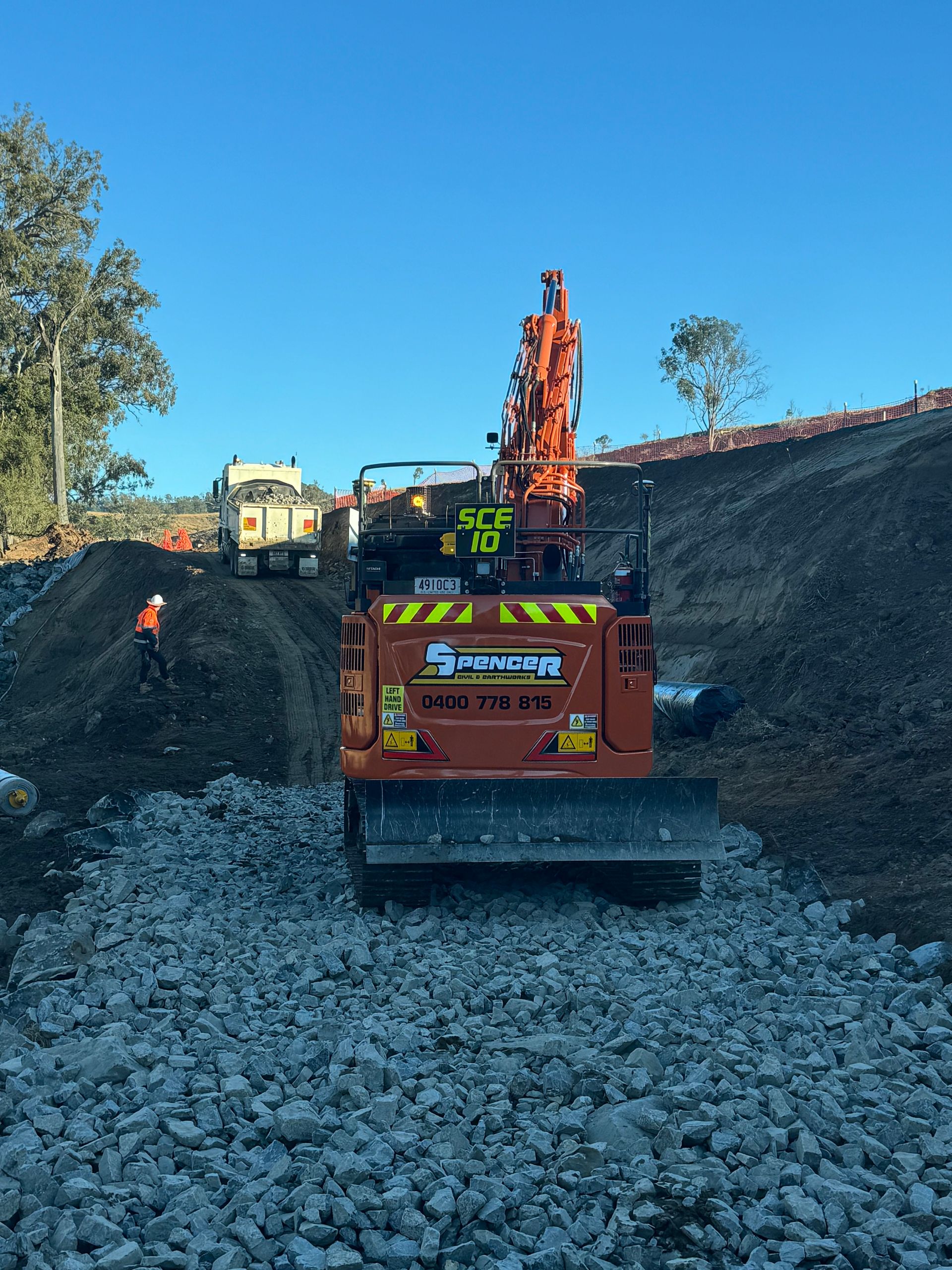 A spencer civil & earthworks excavator is reinforcing a dirt path  with rocks to improve traction.