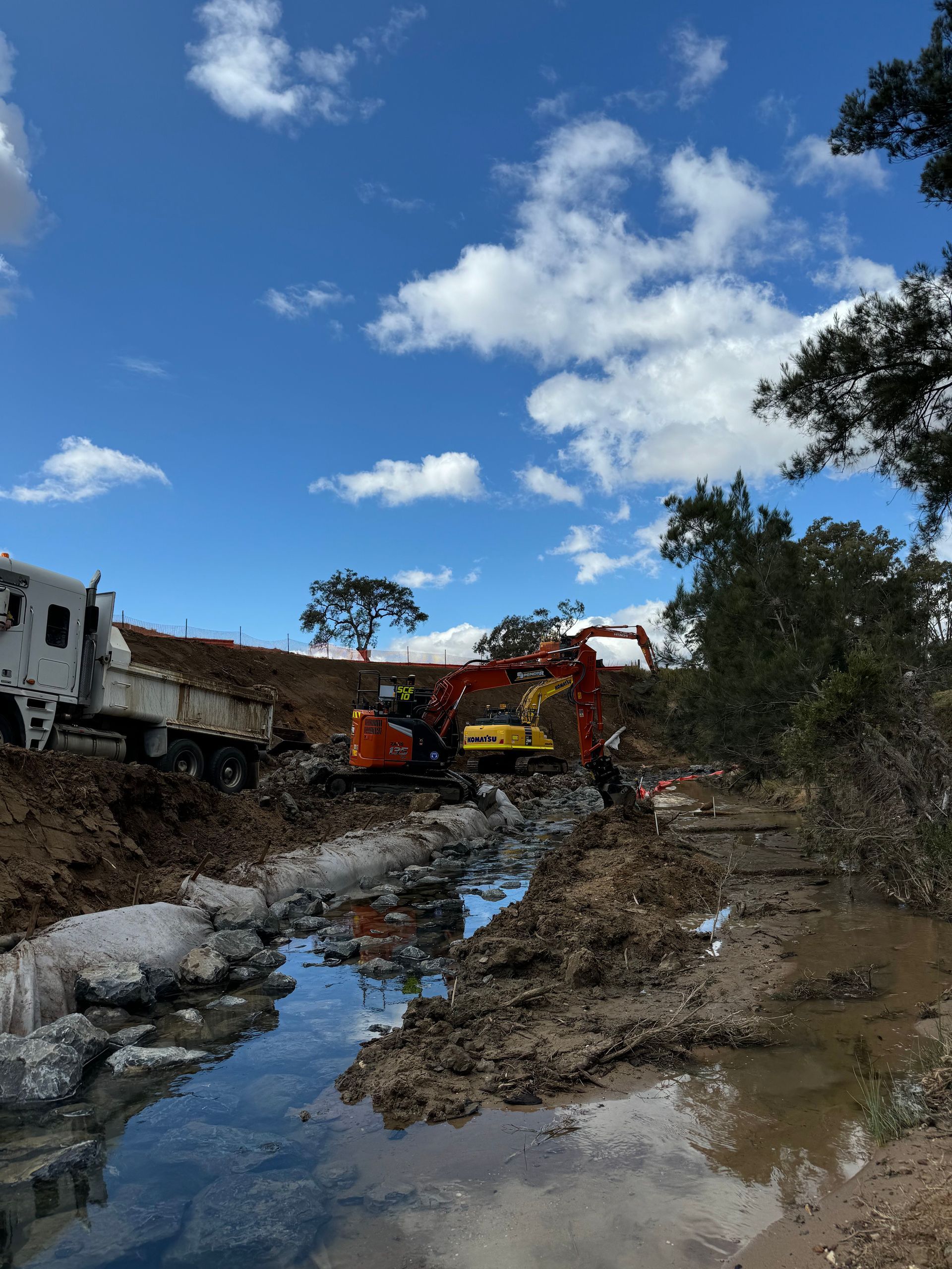 Two Spencer Civil & Earthworks excavators are working in a muddy river.